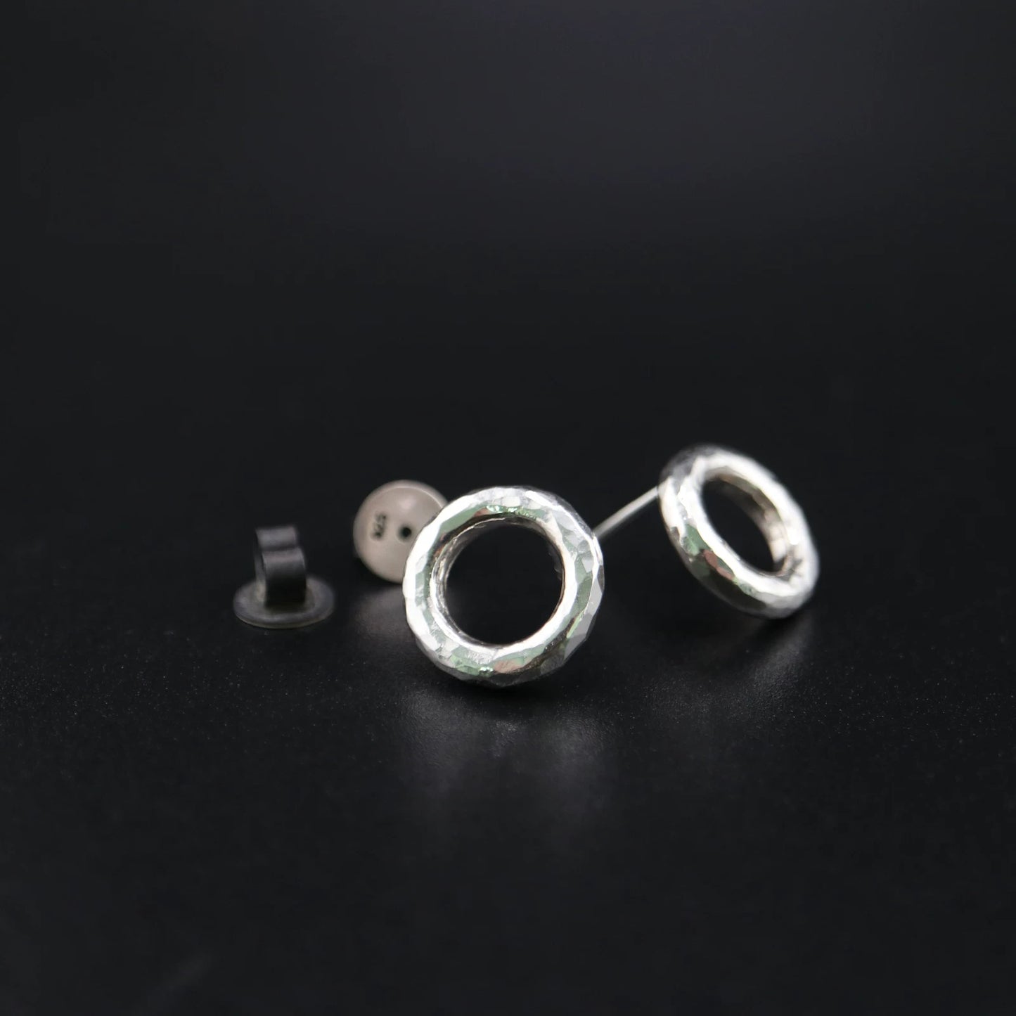 Handmade 925 sterling silver circular stud earrings with a hammered industrial texture and oxidized silver finish.