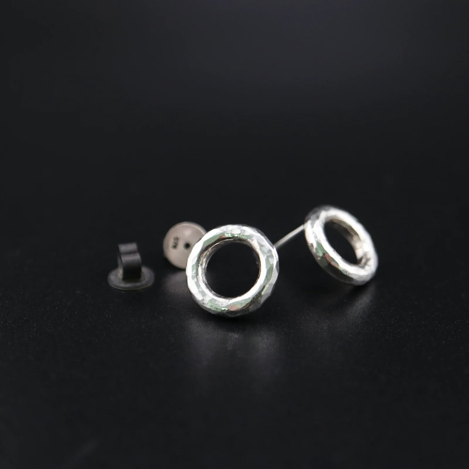 Handmade 925 sterling silver circular stud earrings with a hammered industrial texture and oxidized silver finish.